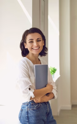 A beautiful smiling girl student stands sideways at the window against the background of the school board. Concept for the start of training sessions. Copy space for ad