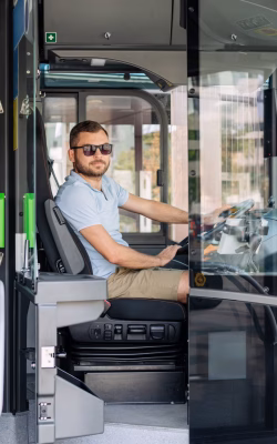 Young adult man city shuttle bus driver sits in driver's cabin while waiting passengers at the bus stop.