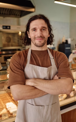 Bakery worker confidently standing against counter with arms crossed and looking at camera